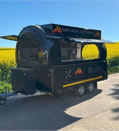 Schwarzer Foodtruck mit Feuerdesign und Schriftzug 'Geht nicht, gibts nicht' vor gelbem Rapsfeld unter blauem Himmel