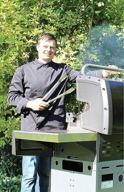 Mann grillt im Garten an einem modernen Gasgrill mit Grillzange in der Hand