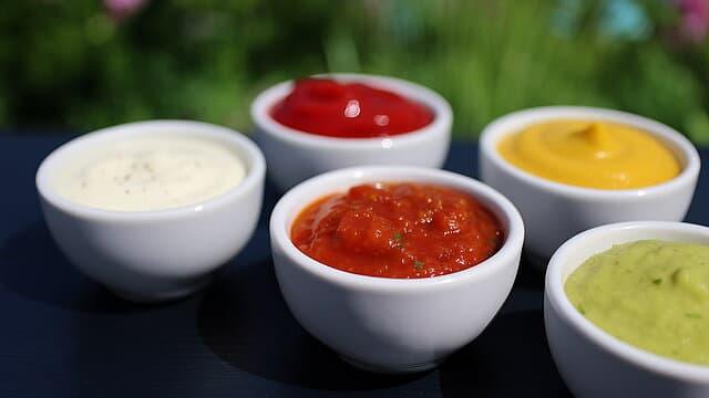 Fünf Schälchen mit verschiedenen Grillsaucen auf schwarzem Tisch.