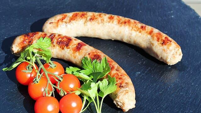 Zwei gegrillte Bratwürste mit Cocktailtomaten und Petersilie.