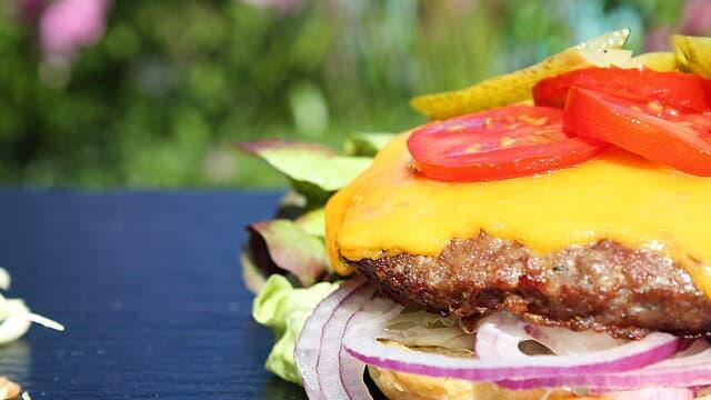 Offener Cheeseburger mit Rindfleisch, Tomate, Zwiebeln und Salat.