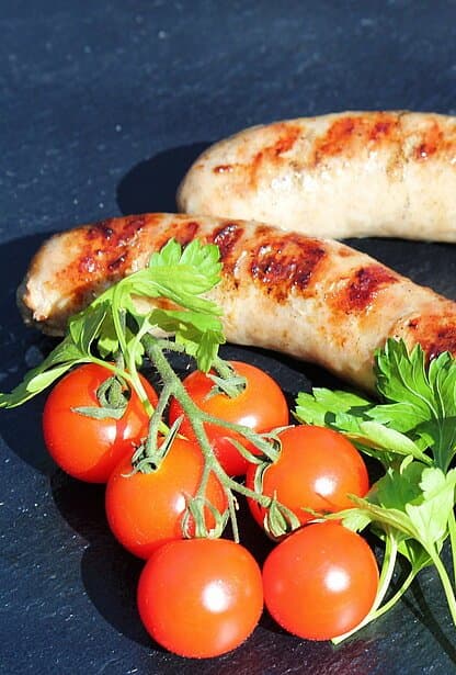 Zwei Bratwürste mit Grillstreifen, daneben frische Cherrytomaten und Petersilie.