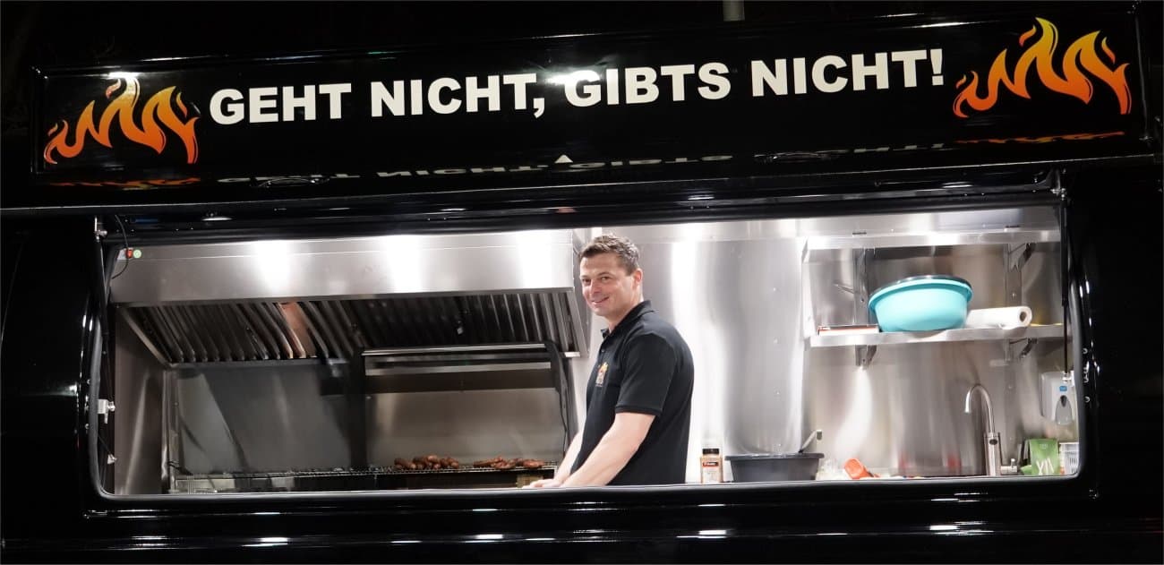 Herr Bayer steht hinter dem Grill seines Foodtruck.